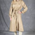 Front view of the BLIZZARD women’s trench coat pattern in beige fabric, with the tie belt defining the waist and one hand on the hip.