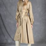 Three-quarter side view of the BLIZZARD beige hooded raincoat sewing pattern, showing the hood raised and the waist belt tied.