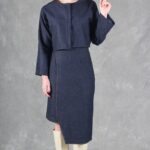 JANYS asymmetrical pencil skirt sewing pattern, front view with a dark navy matching cropped jacket and cream knee-high boots.