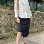 JANYS asymmetrical denim pencil skirt sewing pattern styled outdoors with a loose white blouse and black pointed heels.