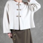 Patrón de costura de chaqueta holgada VALENTINE: vista frontal de la chaqueta crema con botones y falda midi oscura.