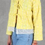 Patrón de costura de chaqueta corta VALENTINE: detalle de la chaqueta amarilla con lazos y encaje blanco en el bajo.
