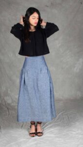 Modelo luciendo una falda confeccionada con el Patrón de Falda Fruncida para Principiantes "Noa", en tela de chambray azul. La prenda destaca por su canesú ancho, frunces sutiles y silueta evasé, ideal para costureras principiantes.