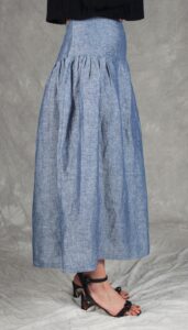 Modelo luciendo una falda confeccionada con el Patrón de Falda Fruncida para Principiantes "Noa", en tela de chambray azul. La prenda destaca por su canesú ancho, frunces sutiles y silueta evasé, ideal para costureras principiantes.