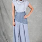 Patrón de costura de falda asimétrica MILLISIERES: falda larga azul pálido con canesú diagonal gris, modelo con una mano en la cadera.