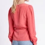 AGATHE blouse sewing pattern: three-quarter back view of the coral-pink blouse showing shoulder gathers, long sleeves and a shaped waist.