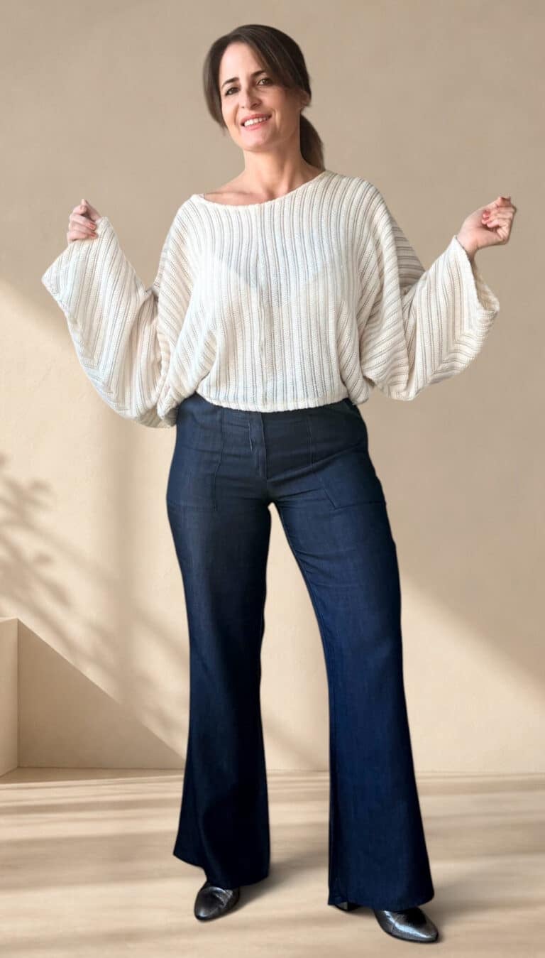 Patrón de costura pantalón acampanado AUDE: mujer sonriente con los brazos en alto, jersey blanco de mangas anchas