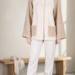 JOY high-neck jacket sewing pattern: front view of a cream and beige raglan-sleeve jacket worn with light trousers.