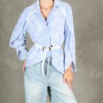 GALATEE floral shirt sewing pattern: front view of the pale-blue long-sleeved shirt cinched with a white belt over light jeans.