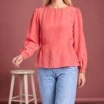 AGATHE long-sleeve blouse sewing pattern: front view of the coral-pink blouse with gathered shoulders, worn with jeans.